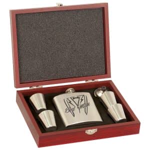 A metal flask set with four cups and a funnel in a red box; flask features a black design. Product: 7092.