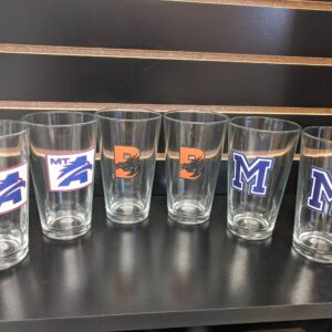 Six Import placeholder for 13469 glasses with assorted college logos are lined up on a shelf against a black background.