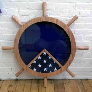 Import placeholder for 1505, a folded American flag in a wooden ship wheel frame, leans on a white brick wall and wood floor.