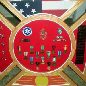 Import placeholder for 386: Display case with military medals, badges, flag, patch, and engraved nameplate on red background.